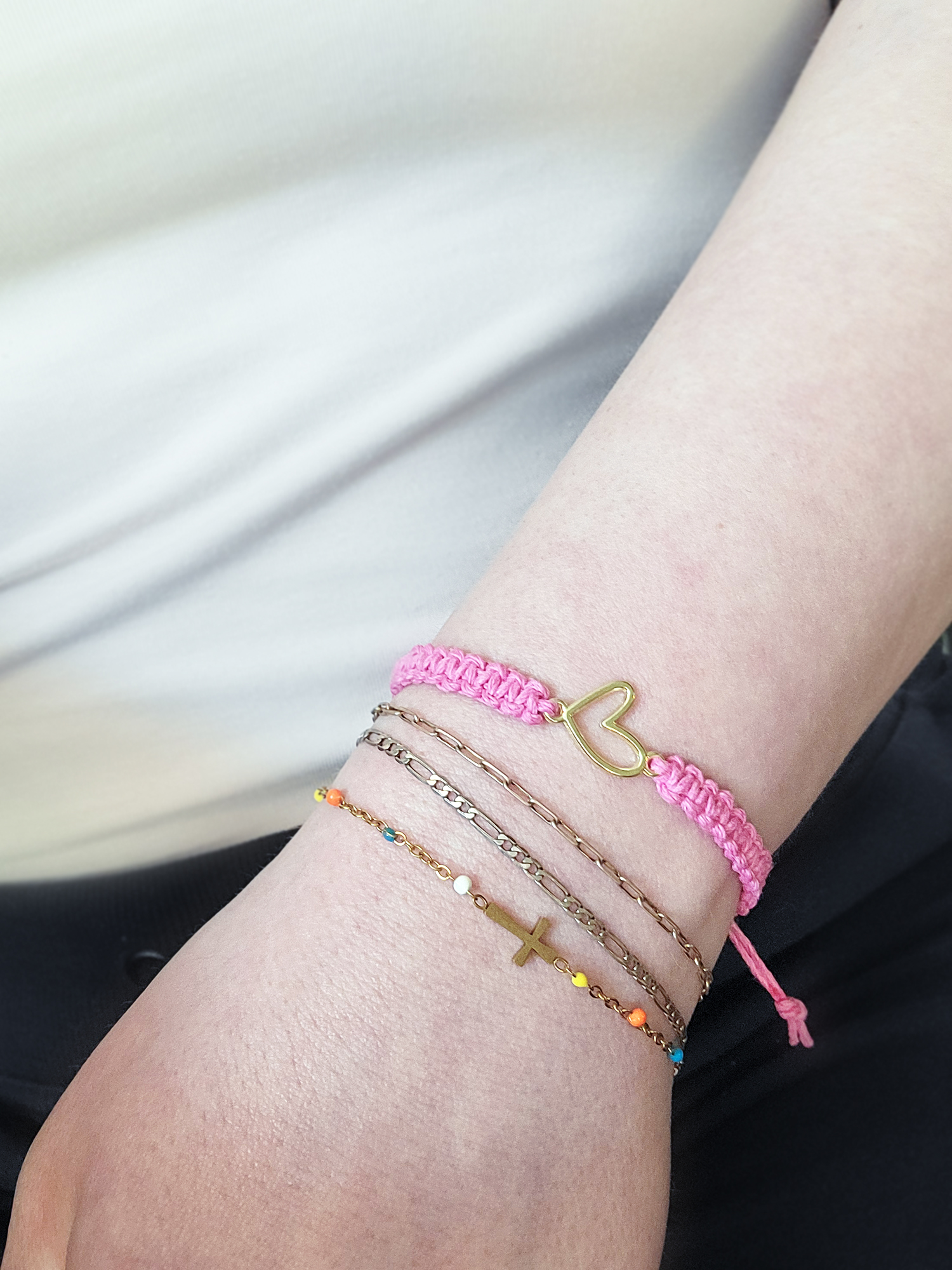 Pink hemp bracelet with gold heart charm worn on wrist with layered gold bracelets.