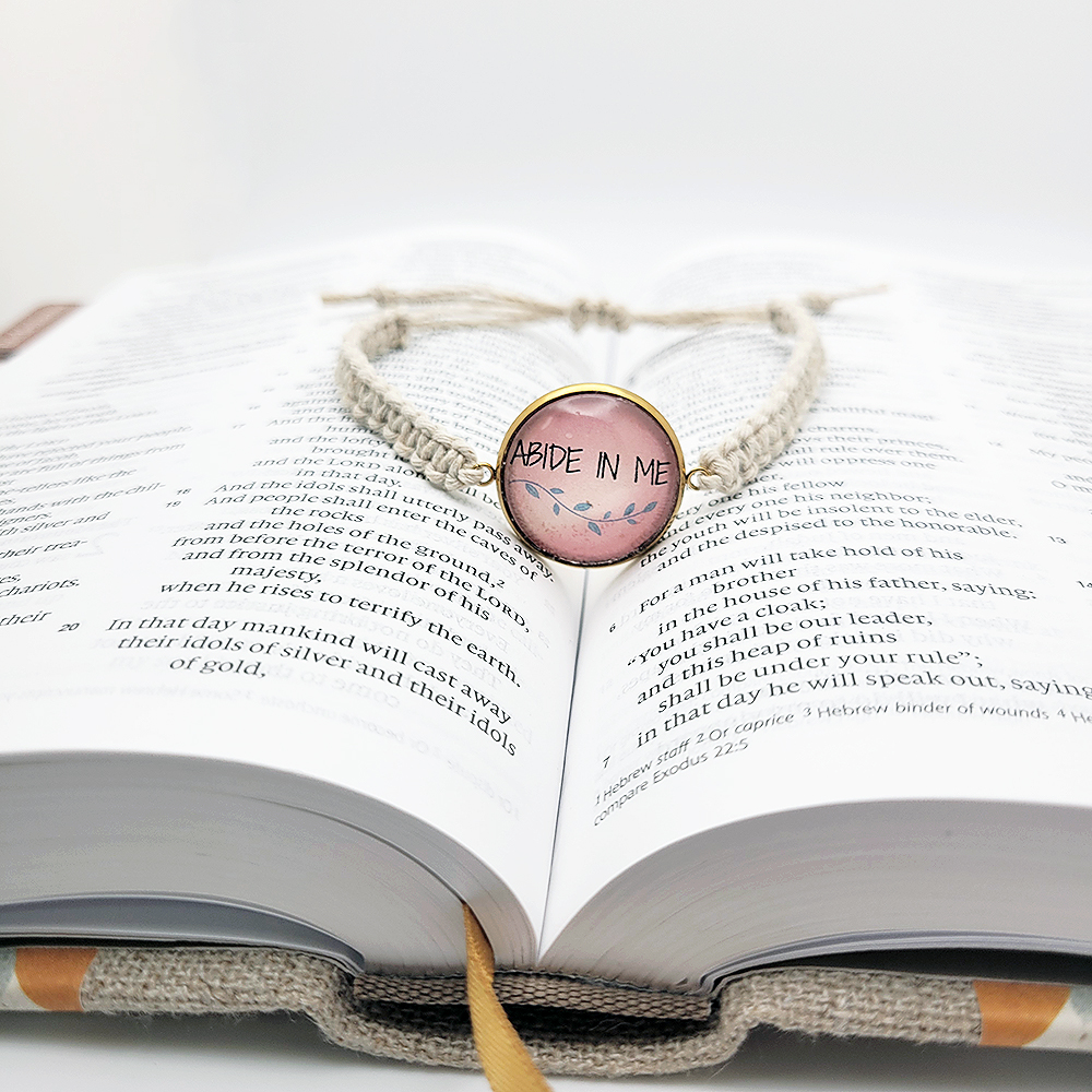 Abide in Me hemp bracelet with pink scripture cabochon and natural cord, Christian bracelet inspired by John 15:4 sitting on Bible.