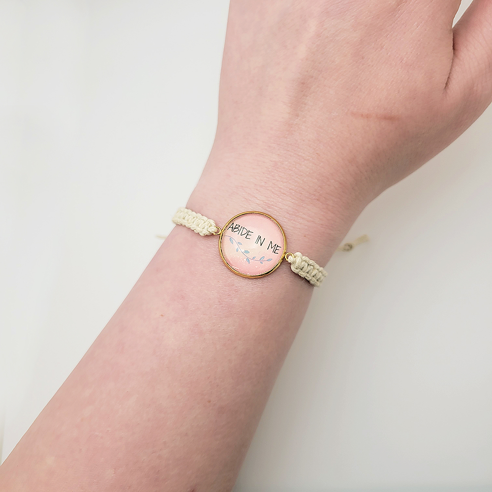 Pink Abide in Me cabochon bracelet on natural hemp cord with gold bezel, handmade Christian jewelry on wrist