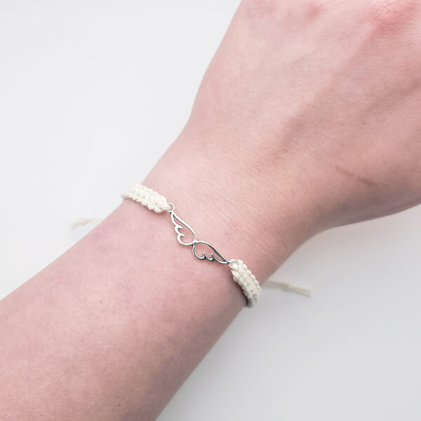 Handmade angel wings hemp bracelet with silver charm worn on wrist, faith-inspired jewelry by Faith & Fiber Studio.