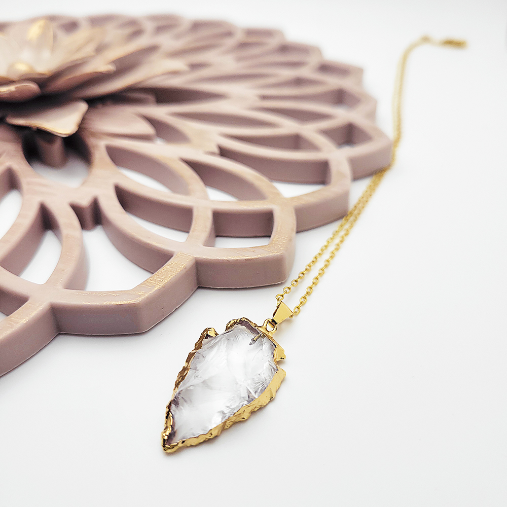 Gold arrowhead quartz pendant necklace displayed on pink jewelry tray