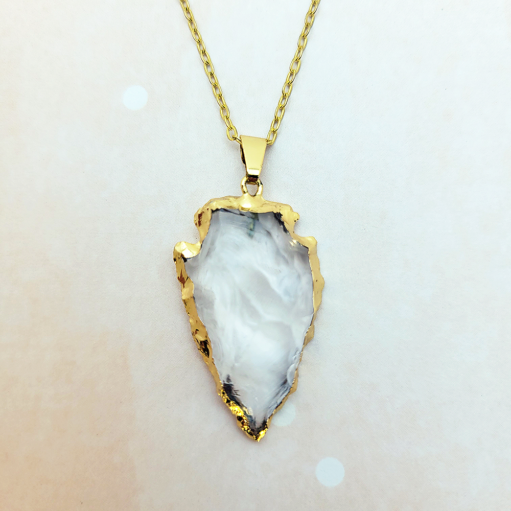Close-up of gold arrowhead clear quartz pendant on delicate gold chain