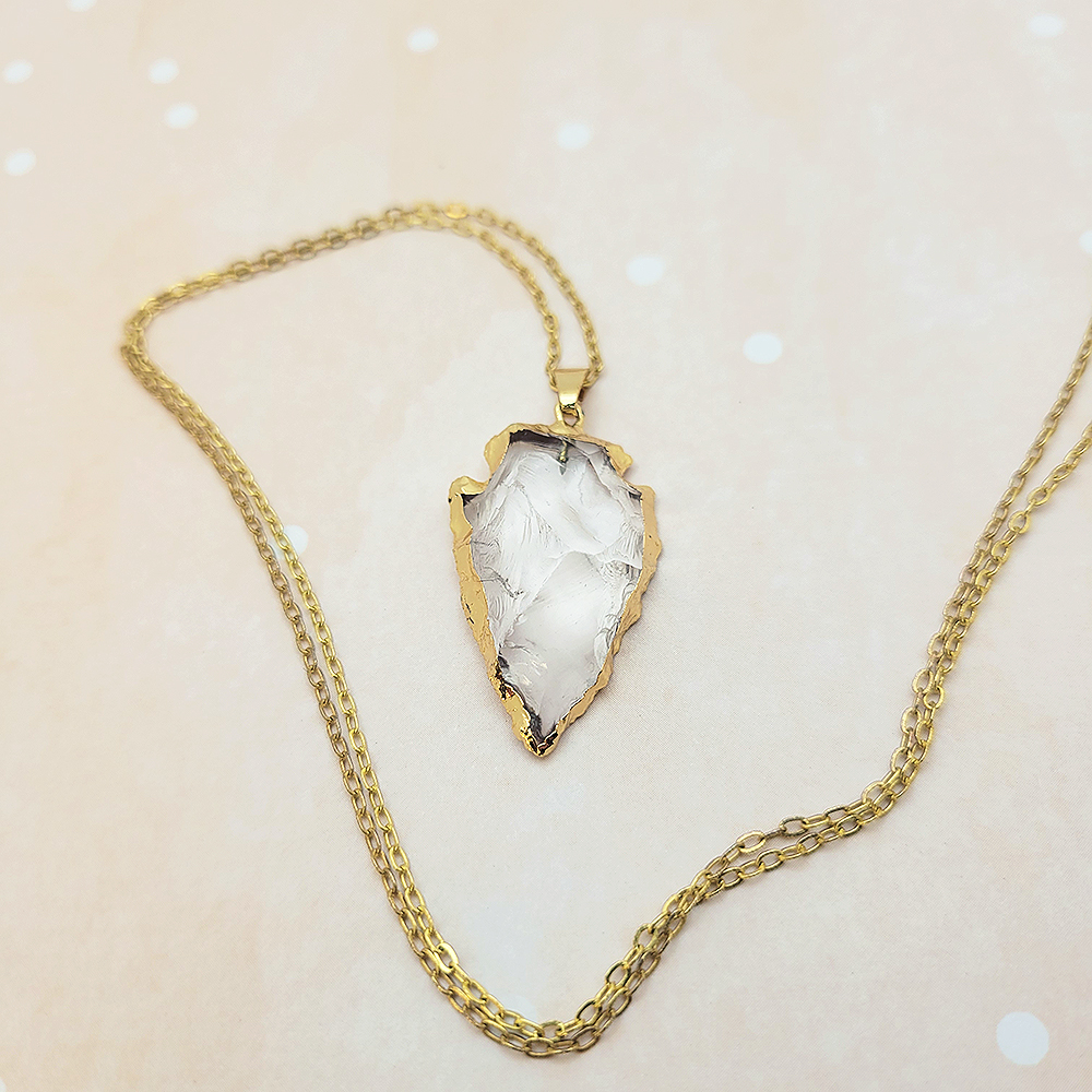Gold arrowhead clear quartz necklace styled on soft neutral background