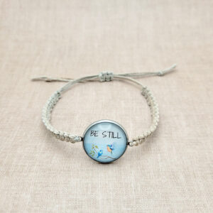 Handmade hemp bracelet with “Be Still” bluebird design on natural linen background, featuring silver bezel and neutral cord