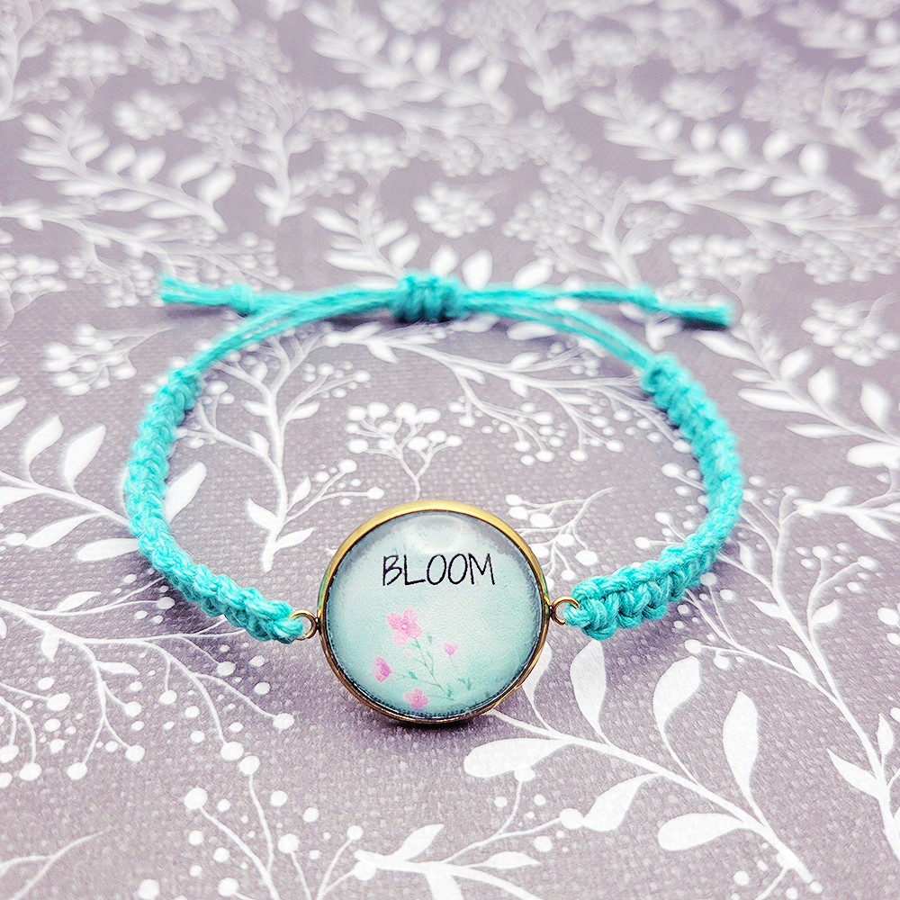 Handmade Bloom bracelet with floral charm on turquoise hemp cord styled on soft floral background, faith inspired jewelry