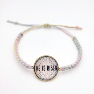 He Is Risen hemp bracelet with pastel multicolor cord and gold bezel on white background, Christian Easter faith jewelry