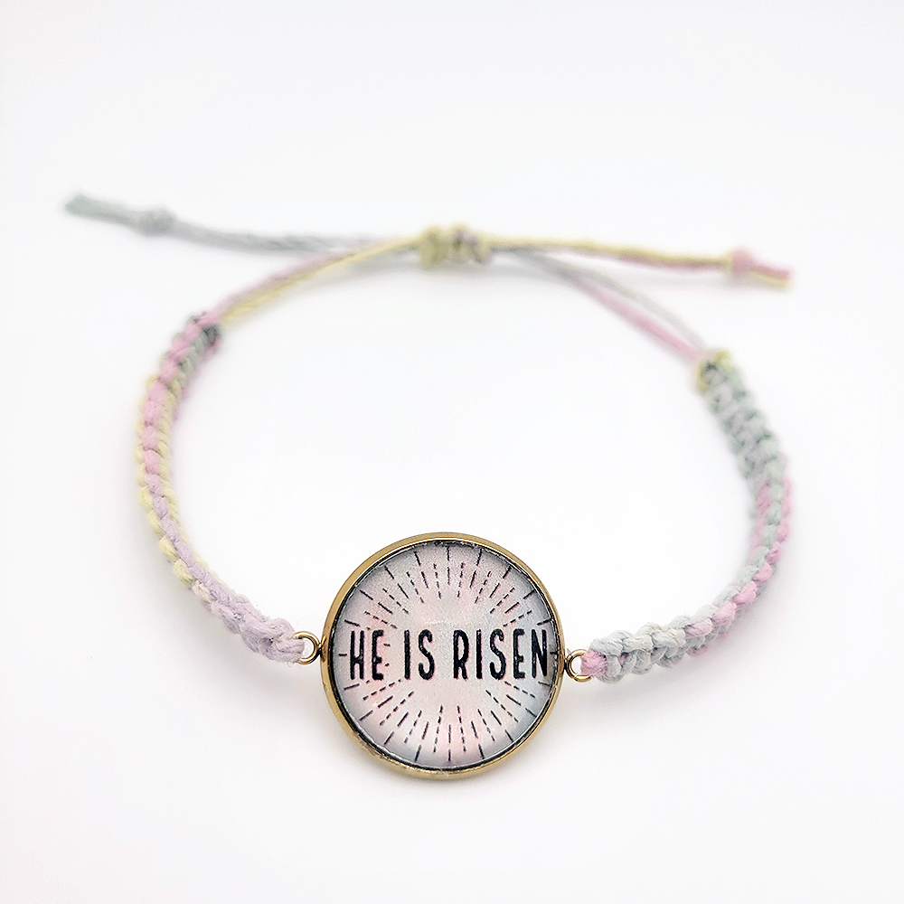 He Is Risen hemp bracelet with pastel multicolor cord and gold bezel on white background, Christian Easter faith jewelry