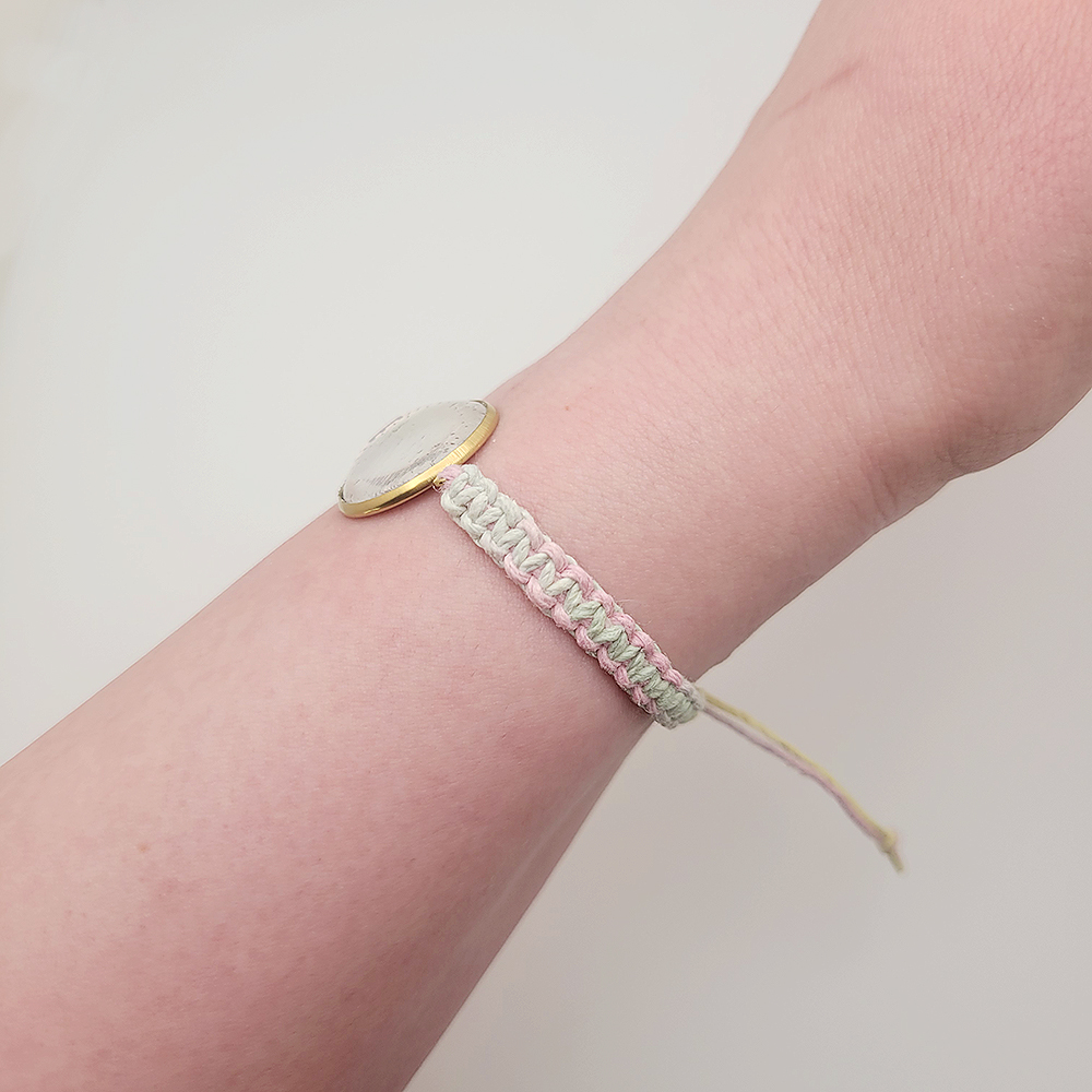 Side view of He Is Risen bracelet on pastel hemp cord showing braided detail and gold setting, Christian faith jewelry