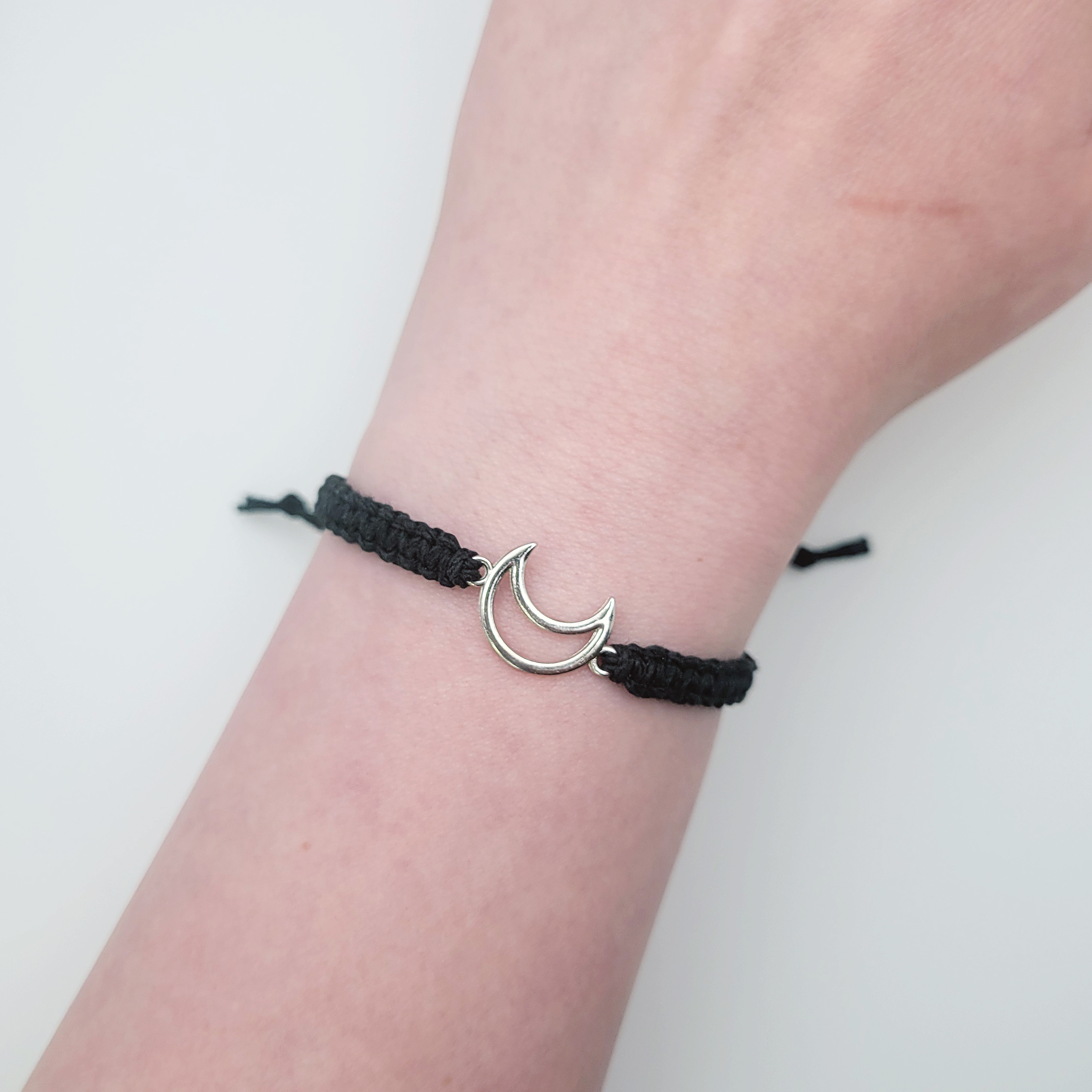 Moon charm hemp bracelet worn on wrist, adjustable black cord with silver crescent moon charm