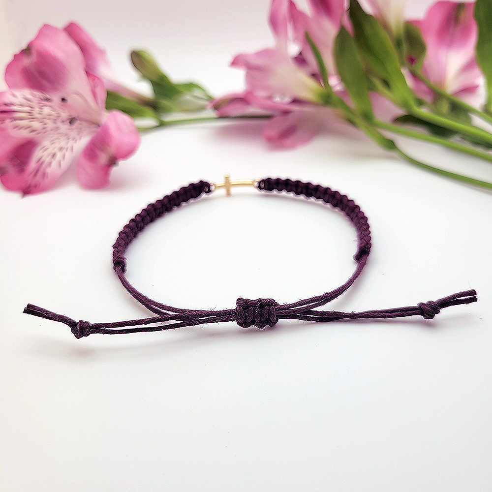 Adjustable sliding knot closure on minimalist gold cross hemp bracelet styled with pink flowers.