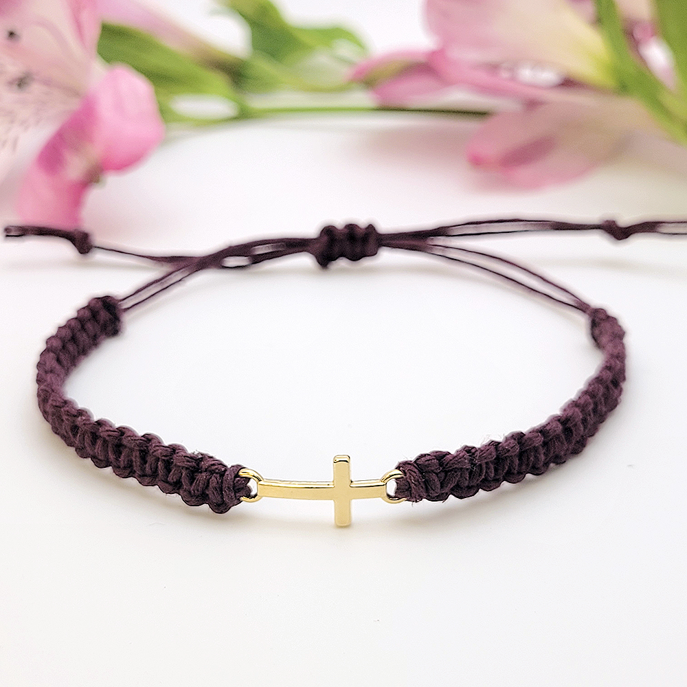 Close-up of small gold cross charm on hand-knotted hemp bracelet
