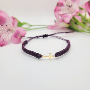 Small gold cross bracelet on burgundy hemp cord with pink flowers in background