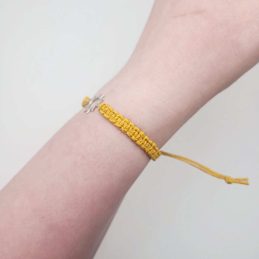 Side view of sun charm hemp bracelet on wrist, adjustable mustard cord with silver sun charm detail