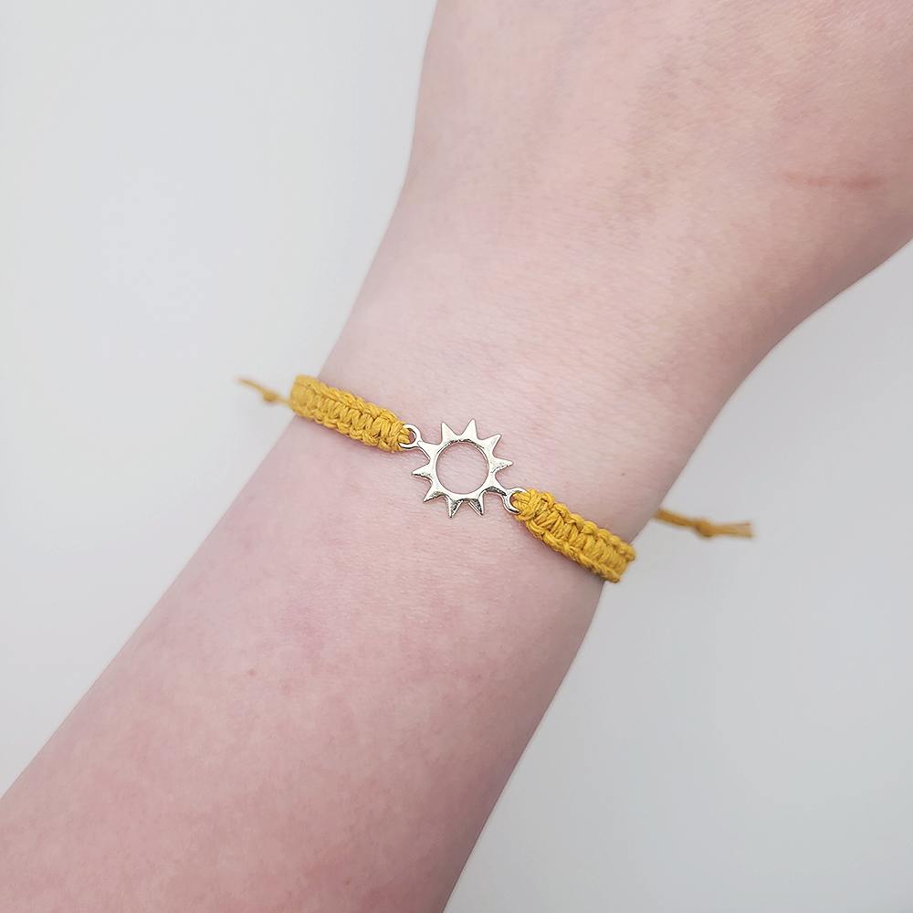 Sun charm hemp bracelet worn on wrist, adjustable mustard yellow cord with silver sun charm