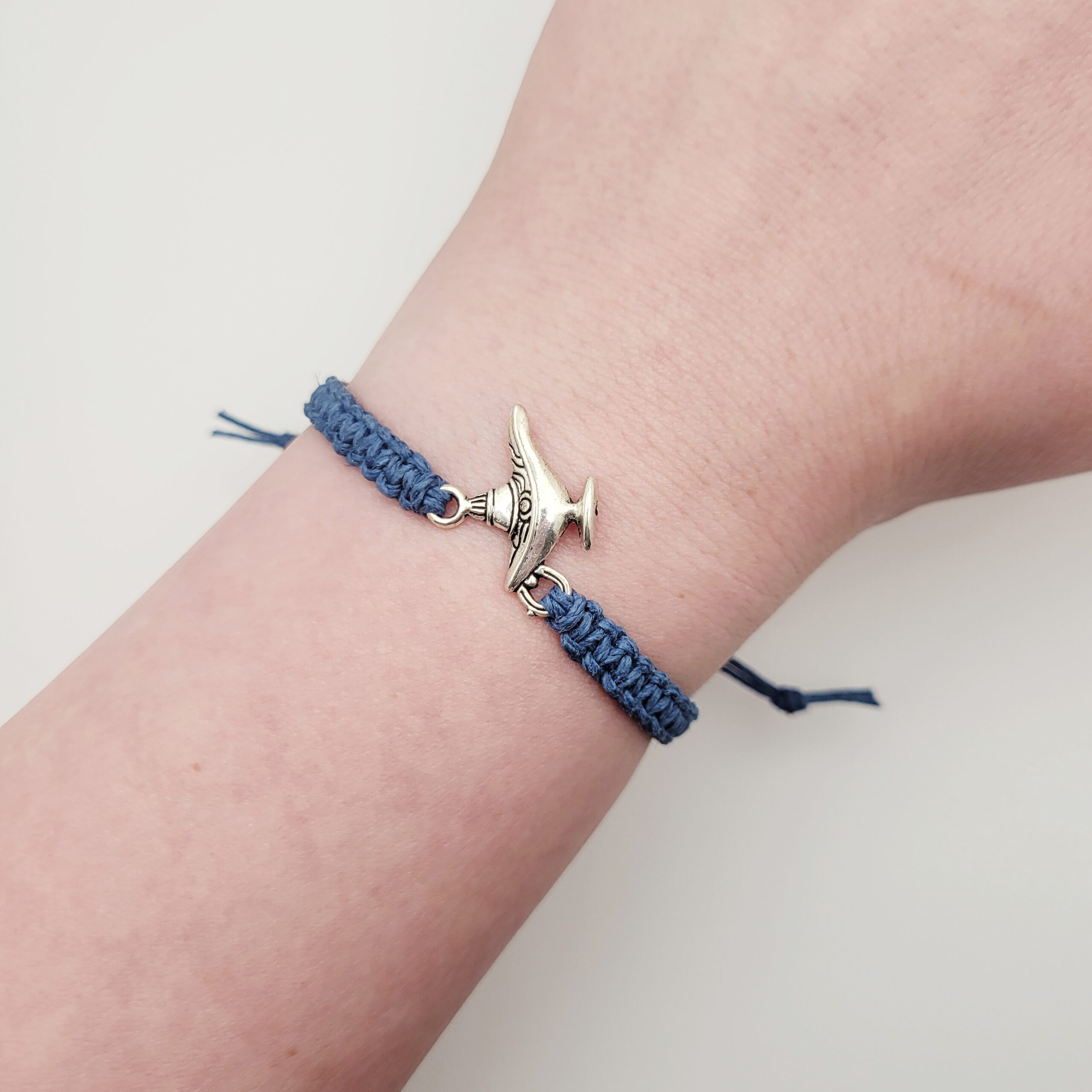 Woman wearing a blue hemp bracelet with a silver lamp charm on wrist, showing the adjustable fit and everyday minimalist style.