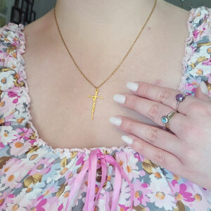 Woman wearing a gold Grace cross necklace while gently holding the pendant.